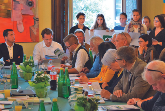 Die Gemeinderät:innen der Stadtgemeinde Gmunden sitzen am Tisch, dahinter stehen Jugendliche von Fridays for Future. Beschlossen wird der Klimapakt.
