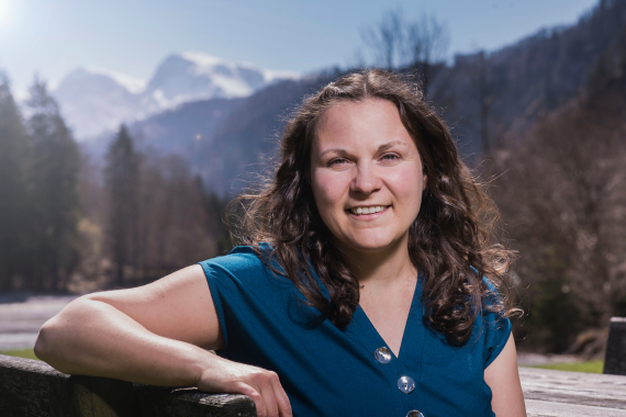 Klimakoordinatorin Verena Pühringer-Sturmayr sitzt an einem Tisch. Im Hintergrund sind Berge zu sehen.