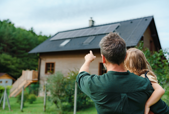 Mann mit Kind auf Arm vor Haus mit Solaranlage