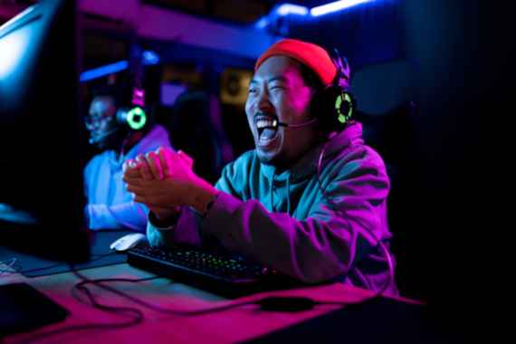 Ein Asiatischer Spieler sitzt vor seinem Gaming-PC und zelebriert seinen Sieg.