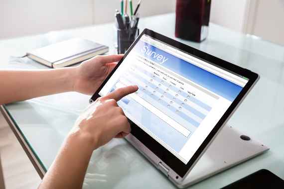 Close-up Of A Businessperson's Hand Filling Online Survey Form On Digital Laptop In Office
