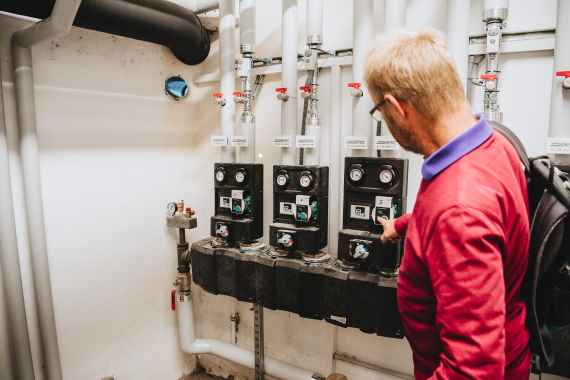 klimaaktiv Heizungs-Check von Energie Tirol: Ein Berater steht im Heizkeller vor einer gedämmten Pumpengruppe und beurteilt die Installation