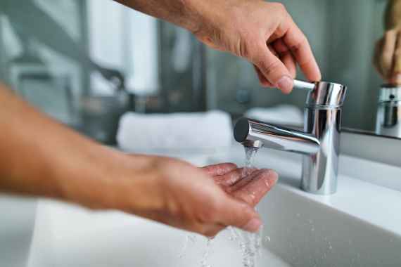 Ein Mann wäscht sich unter rinnendem Wasser die Hände im Waschbecken