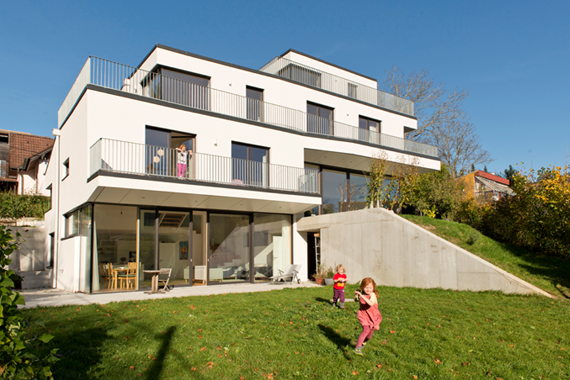 Purkersdorf Passiv-Doppelhaus: Im Hintergrund das 3-stöckige Passivhaus, im Vordergrund spielen 2 Kinder auf einer Wiese