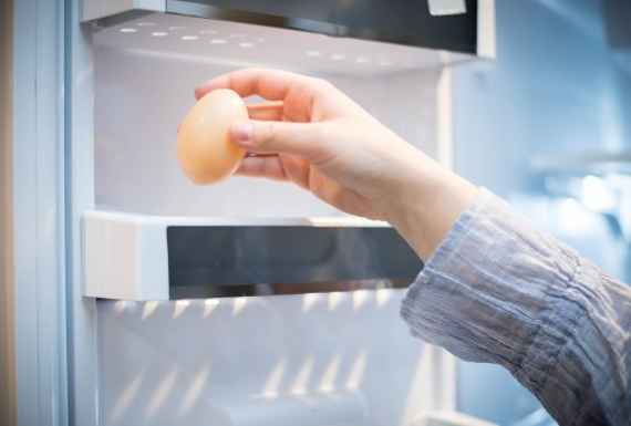 Frau gibt ein Ei in einen Kühlschrank