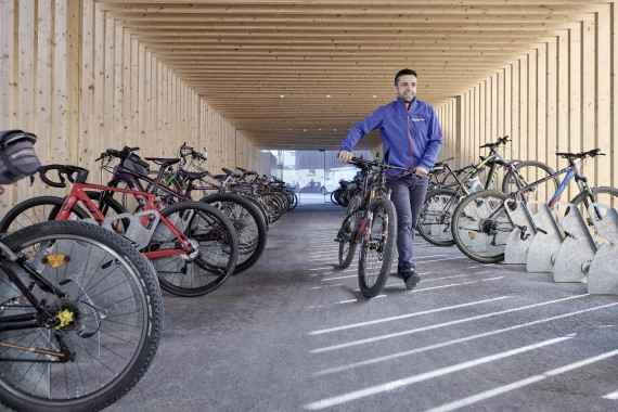 Mann schiebt Fahrrad durch überdachte Fahrradabstellanlage
