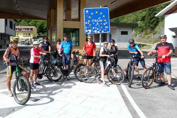 Eine Gruppe Radfahrer:innen posiert für ein Gruppenfoto an der italienischen Grenze.