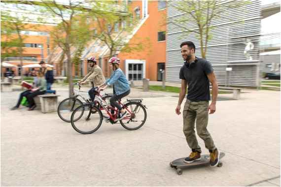 Ein Skateboarder und zwei Fahrradfahrer:innen am Campus der Technischen Universität Graz