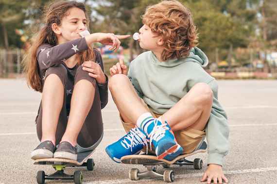 Ein Bub und ein Mädchen sitzen auf Skateboards und spielen mit Kaugummiblasen
