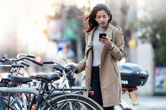 Foto einer jungen Frau, die sich ihre Radfahrroute auf dem Handy anschaut, bevor sie sich auf ihr Fahrrad setzt.
