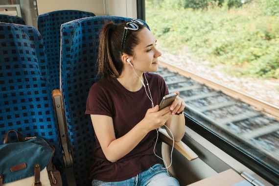 Eine Junge Frau hört beim Zugfahren Musik mit ihrem Handy.