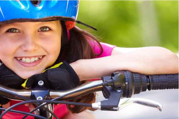 Lachendes Kind lehnt auf Fahrradlenker und trägt einen Helm. 