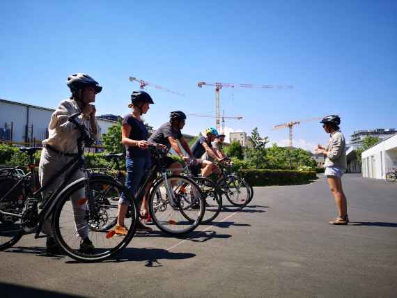 Das Bild zeigt vier Auszubildende des Kurses "Ausbildung klimaaktiv mobil Radfahrlehrende" am Übungsplatz mit Fahrrädern und Radfahrhelm.