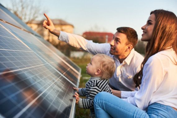 Mutter, Vater und Kind zeigen gemeinsam lächelnd auf eine Photovoltaikanlage