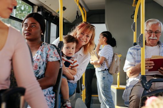 Mutter sitzt im Bus des öffentlichen Verkehrs und hält ein kleines Kind am Schoß.