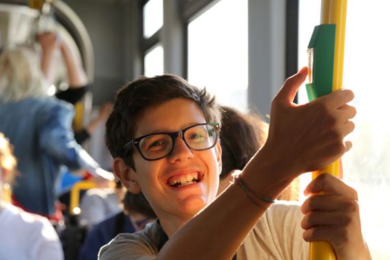 Ein lachender junger Mann mit Brillen fährt mit der Straßenbahn und drückt auf den Haltedruckknopf.