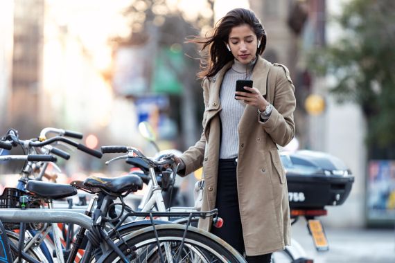Shot of young woman consulting the map on her mobile phone before taking the bicycle on the street.