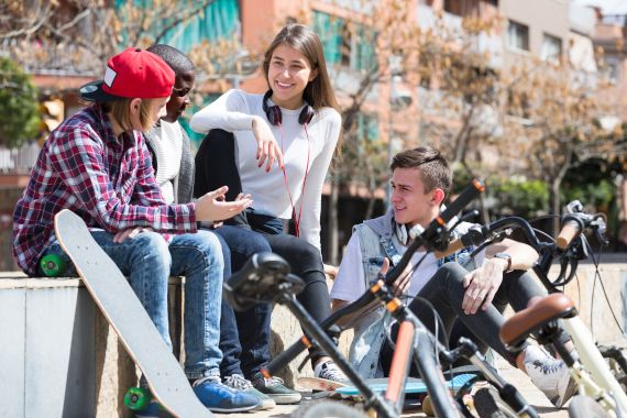 Eine Gruppe Jugendlicher sitzt mit Fahrrädern in der Sonne und plaudert
