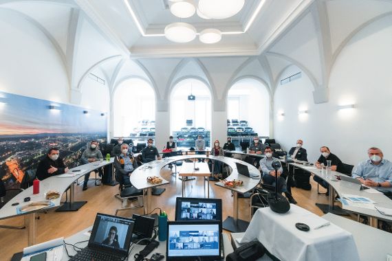 Die Lehrgangsteilnehmer sitzen in einem mit Tischen gebauten Halbkreis im Gemeinderatssaal des St. Pöltner Rathauses. Etwa die Hälfte der Teilnehmer sind online per Video zugeschaltet.