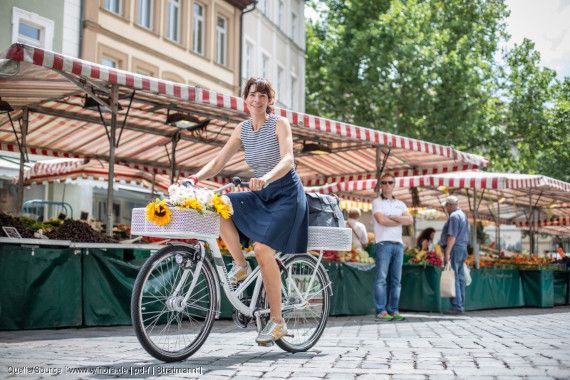 Frau fährt mit einem weißen Fahrrad über einen Marktplatz.