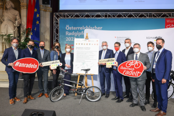 Unterzeichnende halten das Übereinkommen zur Förderung des Radverkehrs auf der Bühne des Radgipfels.