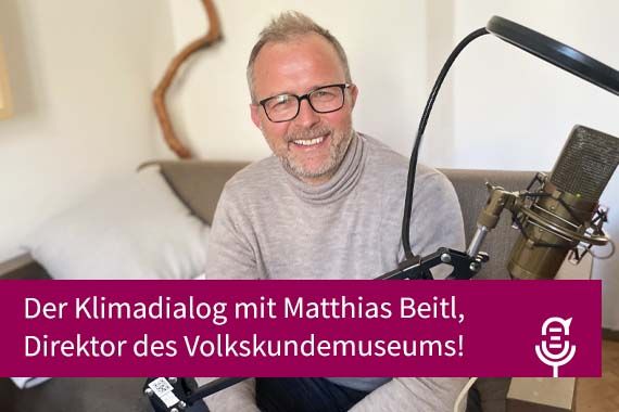 Matthias Beitl lacht vor Podcast-Mikrophon in die Kamera, davor Magenta-farbiger Balken mit Schrift: Der Klimadialog mit Direktor des Vokskundemuseums Matthias Beitl