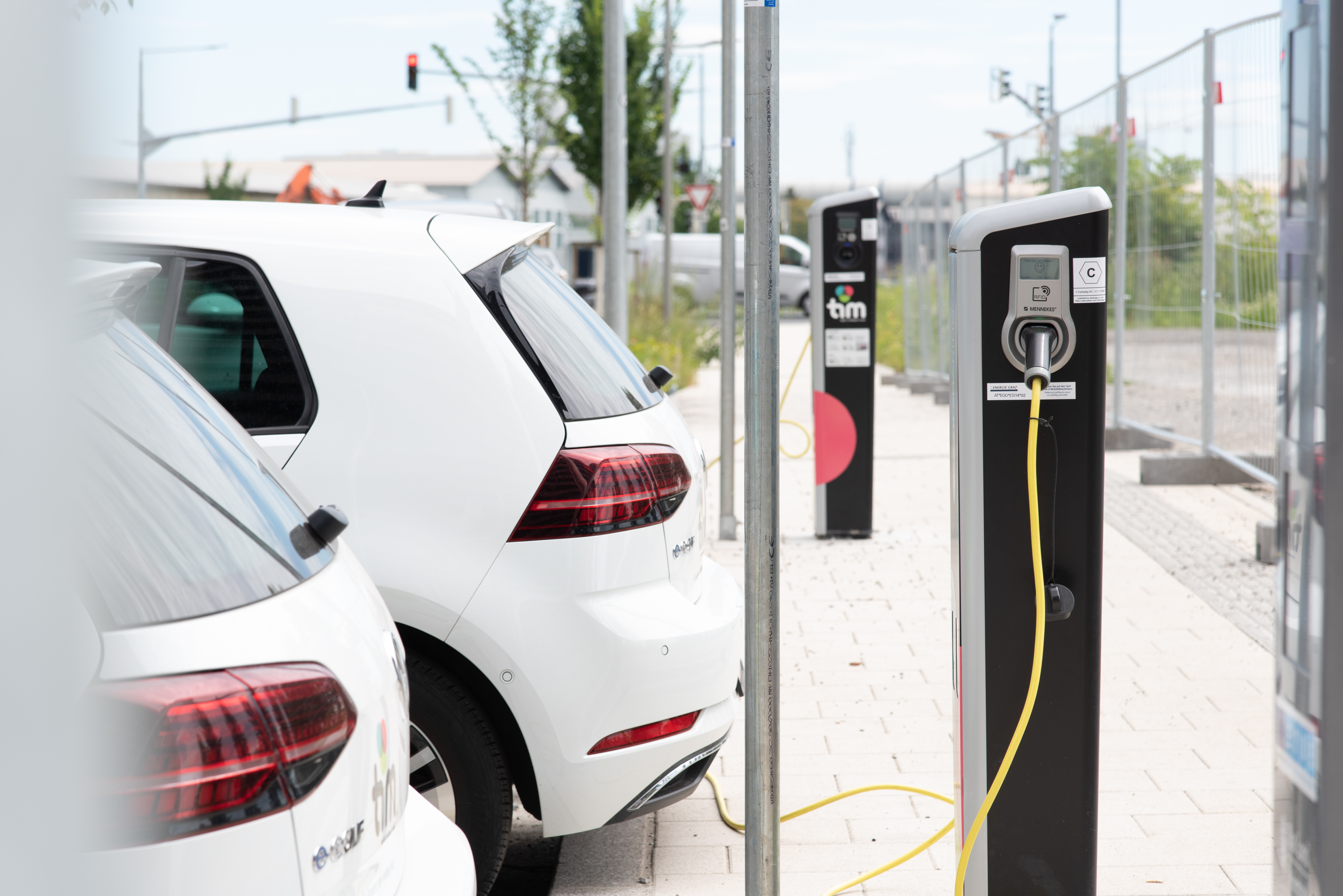 Zwei weiße E-Autos laden gerade mit Kabel an einer Säule auf.