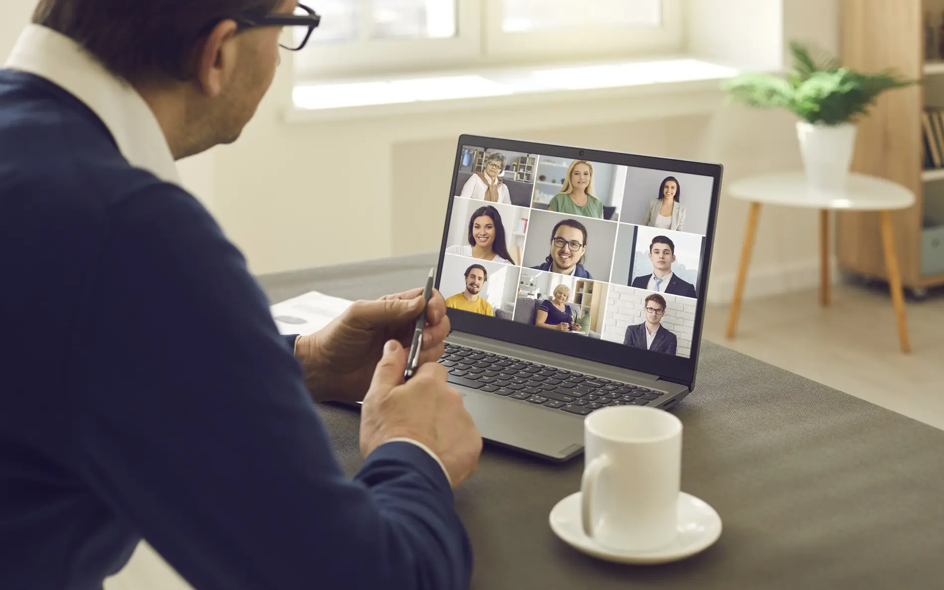 Mann sitzt vor einem Laptop. Am Laptop Screen sieht man einen Videocall mit 9 Personen.
