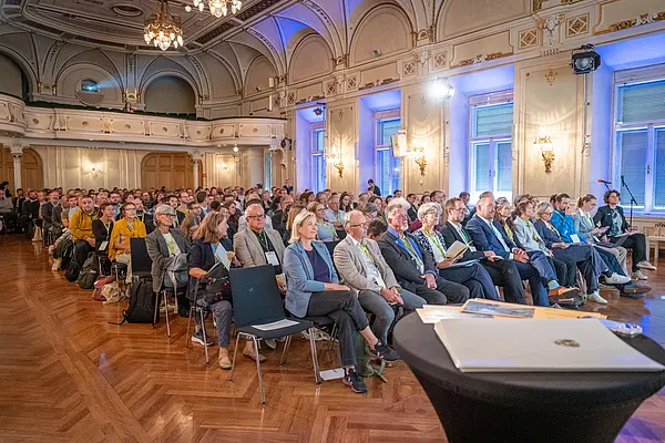 Prunkvoller Saal mit vielen Menschen, die sitzend lauschen