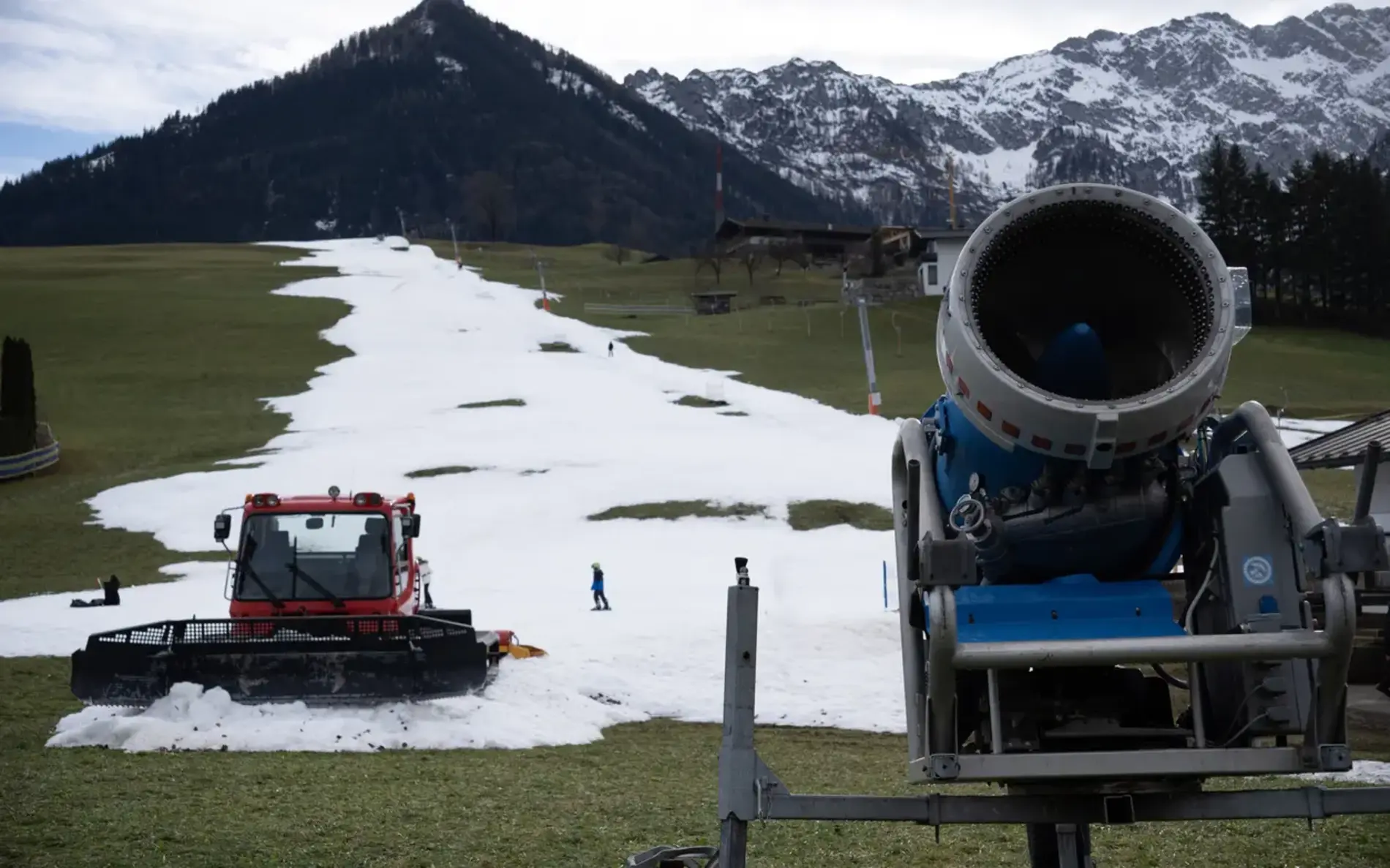 Pistenraupe und Schneekanone auf grüner Wiese.
