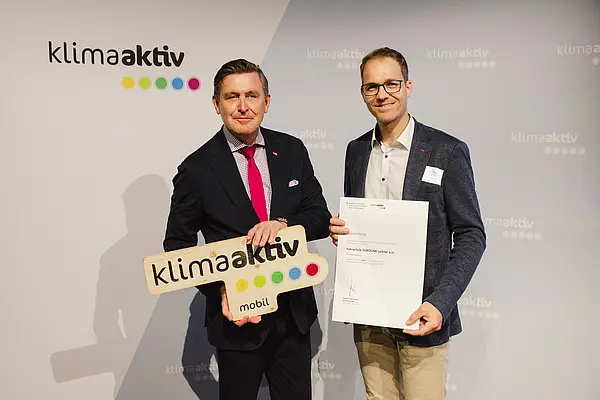 Menschen mit Urkunde und klimaaktiv Schild lächeln in die Kamera