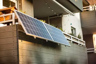 Balkonkraftwerk mit Solarzellen hängt auf einem Balkon aus Beton und ist leicht zur Sonne ausgerichtet.