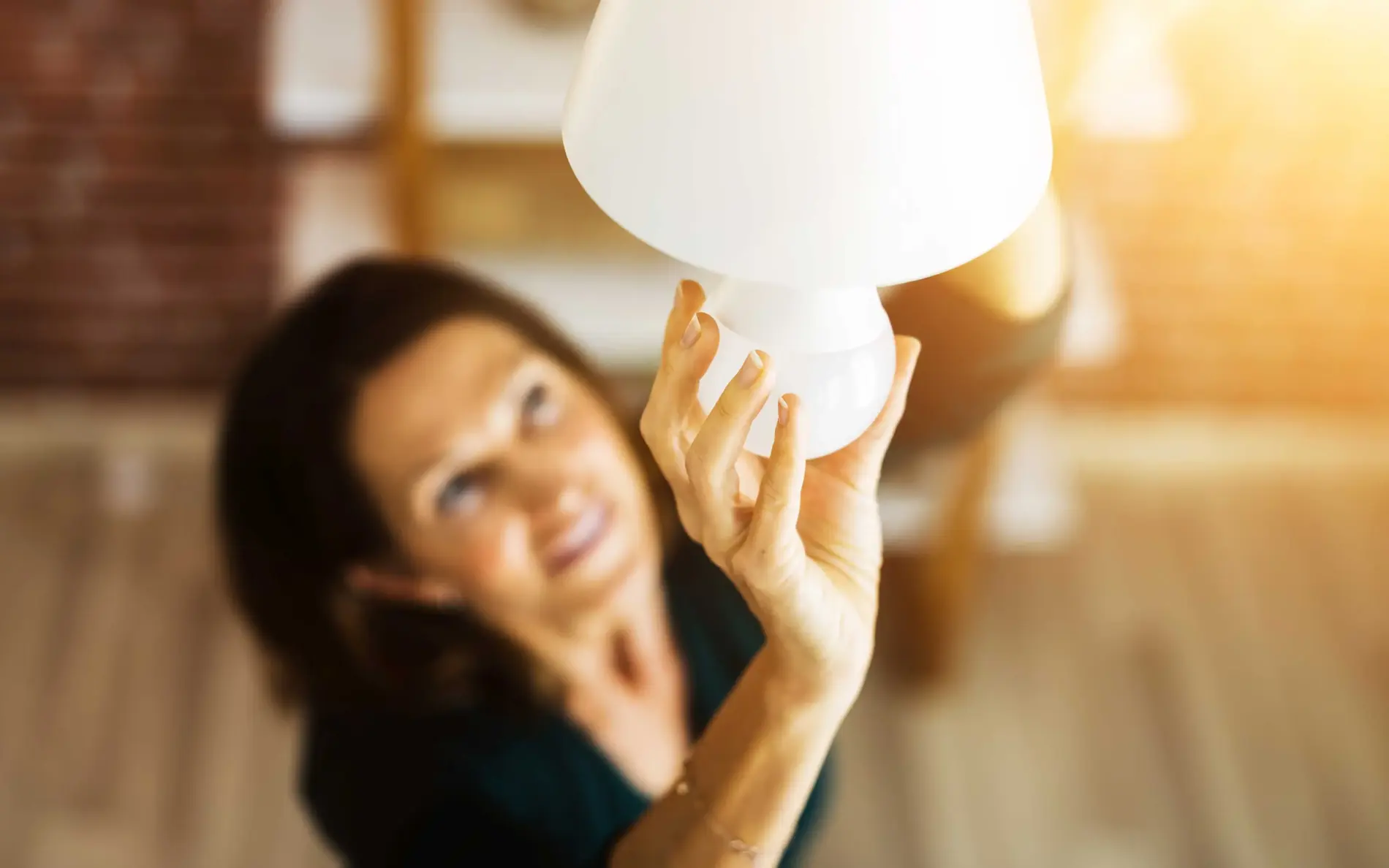 Eine Hand setzt eine weiße Lampenabdeckung auf eine Leuchte in einem hellen Raum.