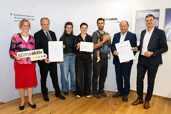 eine Gruppe von Menschen auf einer Bühne hält Urkunden in die Kamera