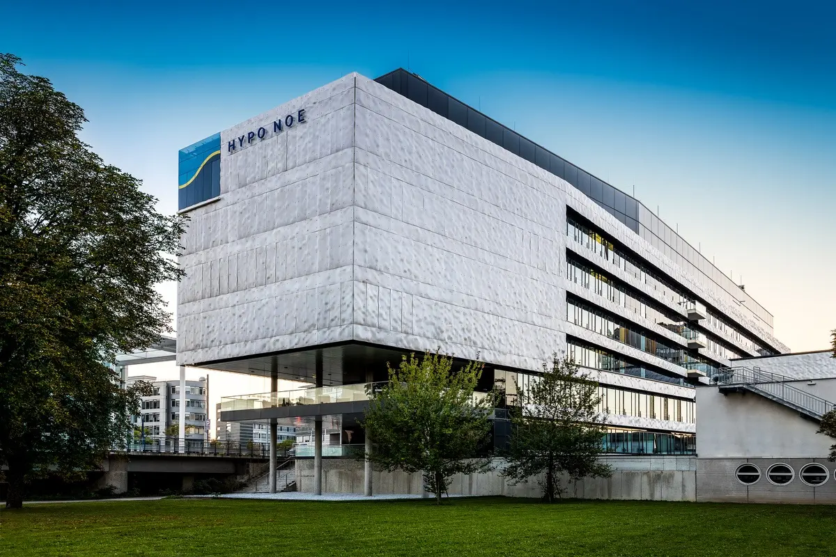 Bürogebäude mit der Aufschrift „HYPO NOE“, umgeben von Grünflächen und Bäumen, bei Tageslicht fotografiert.