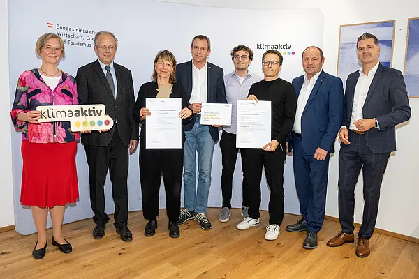 eine Gruppe von Menschen auf einer Bühne hält Urkunden in die Kamera