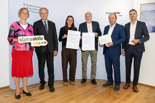 eine Gruppe von Menschen auf einer Bühne hält Urkunden in die Kamera