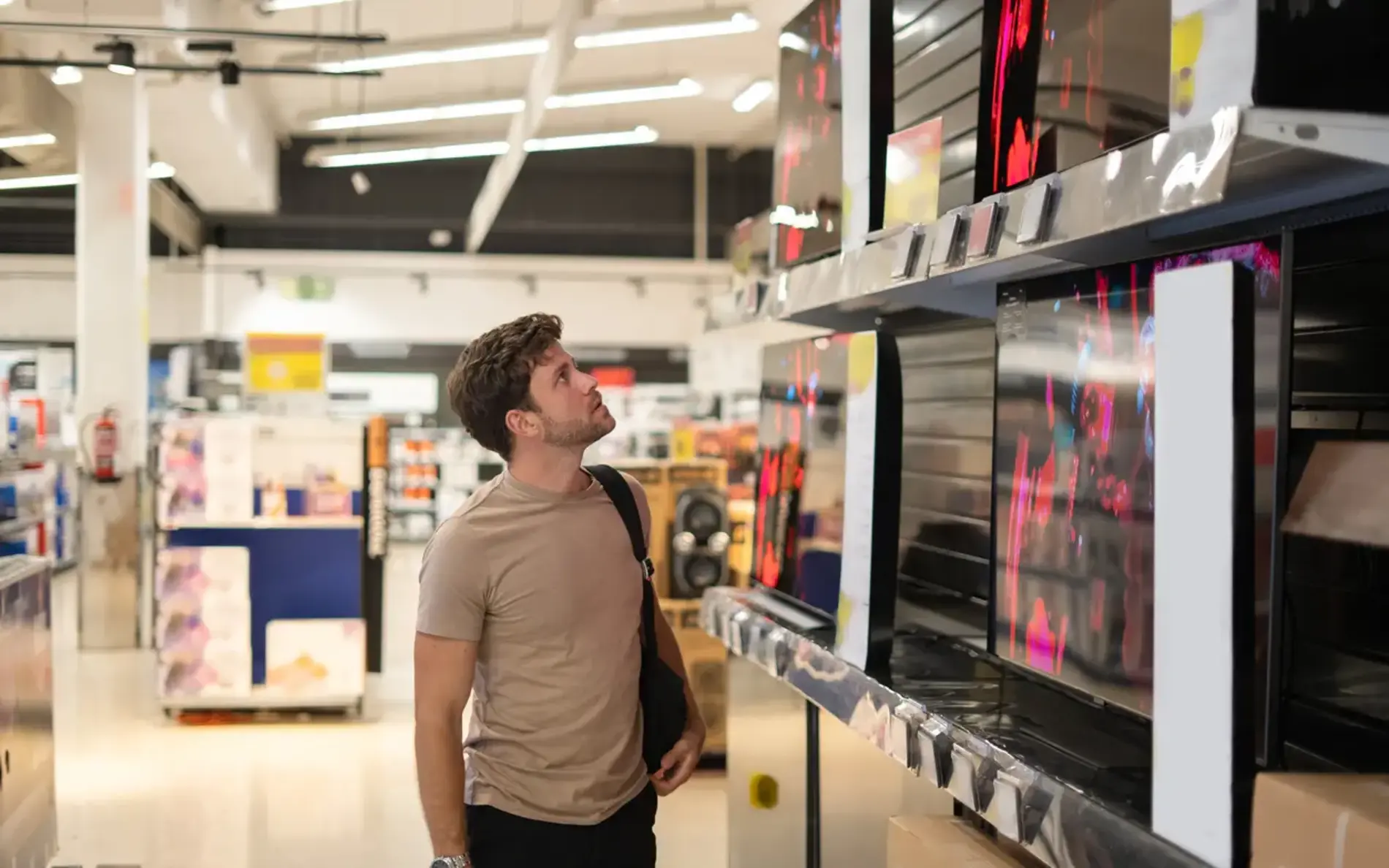 Zu sehen ist ein Mann im Einzelhandel, der sich verschiedenste Fernsehergeräte anschaut.
