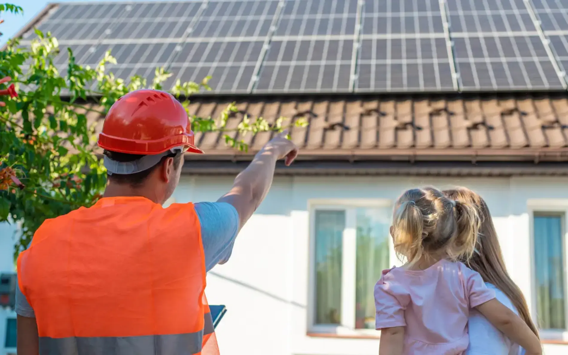 Ein PV-Installateur mit Warnweste und Helm zeigt in Richtung eines PV Daches mit PV-Paneelen. Daneben steht 