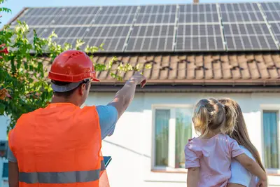 Ein PV-Installateur mit Warnweste und Helm zeigt in Richtung eines PV Daches mit PV-Paneelen. Daneben steht 