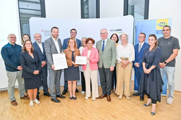 Personen mit Urkunde schauen in die Kamera