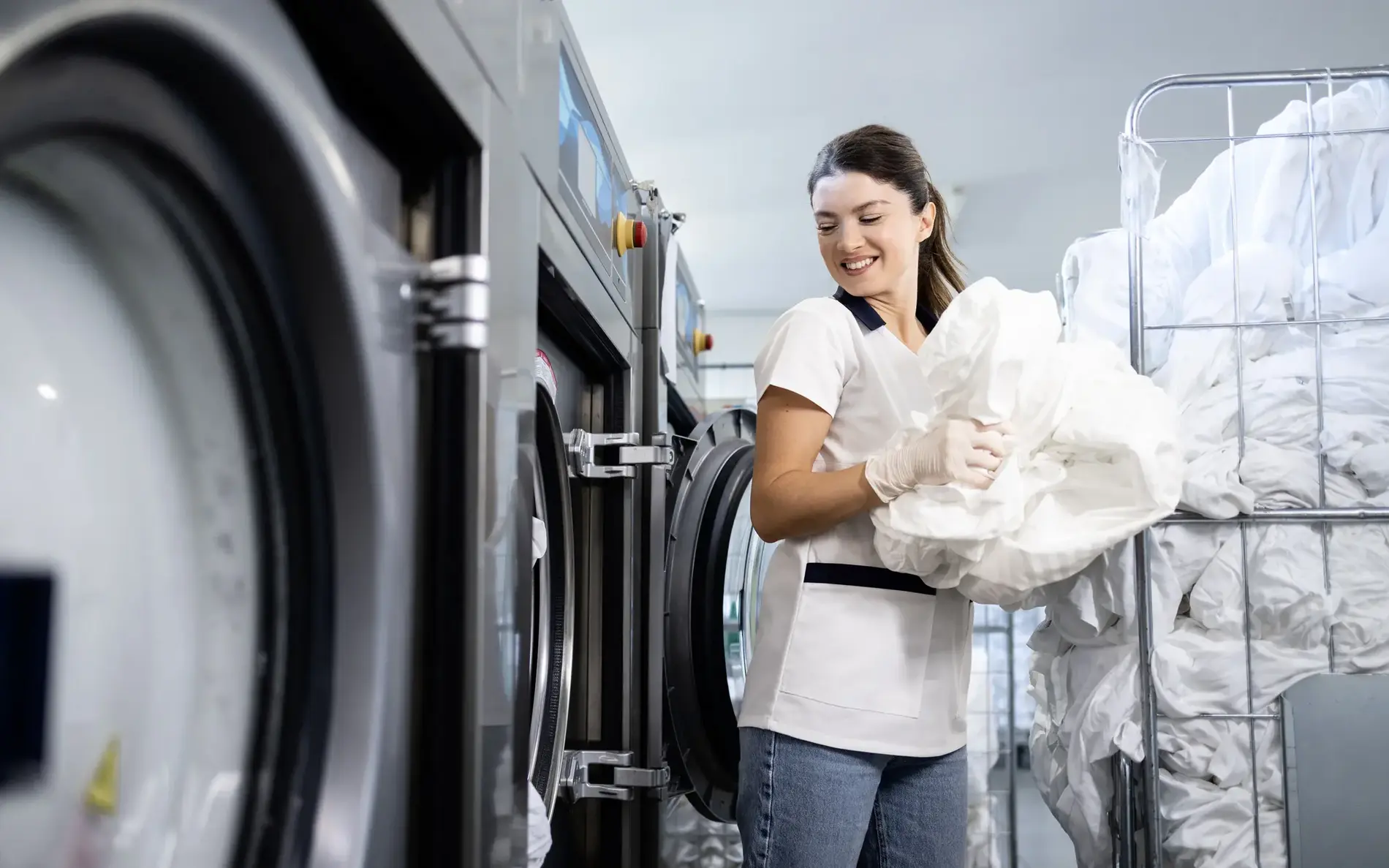 eine Frau in einer professionellen Wäscherei belädt gerade eine Maschine.