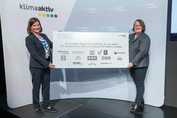 2 Personen halten eine Tafel mit Firmenlogos auf einer Veranstaltung