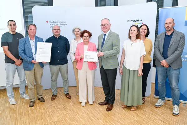 Personen mit Urkunde schauen in die Kamera