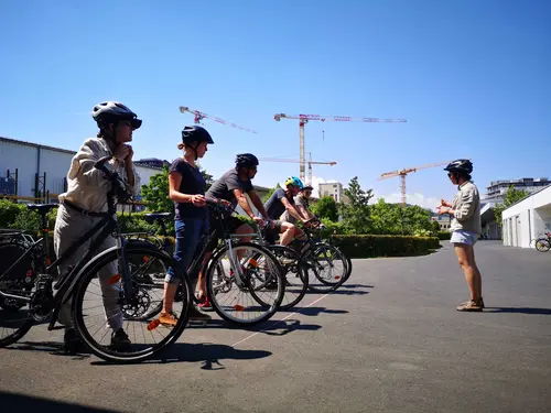 5 angehende Radfahrlehrkräfte mit Fahrrad hören aufmerksam der Vortragenden zu.