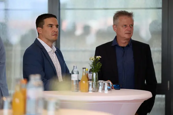 2 Männer auf einer Veranstaltung hören jemandem zu, der nicht im Bild ist