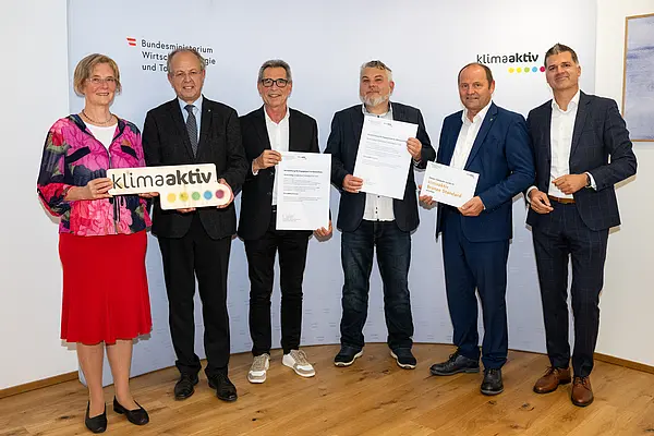 eine Gruppe von Menschen auf einer Bühne hält Urkunden in die Kamera