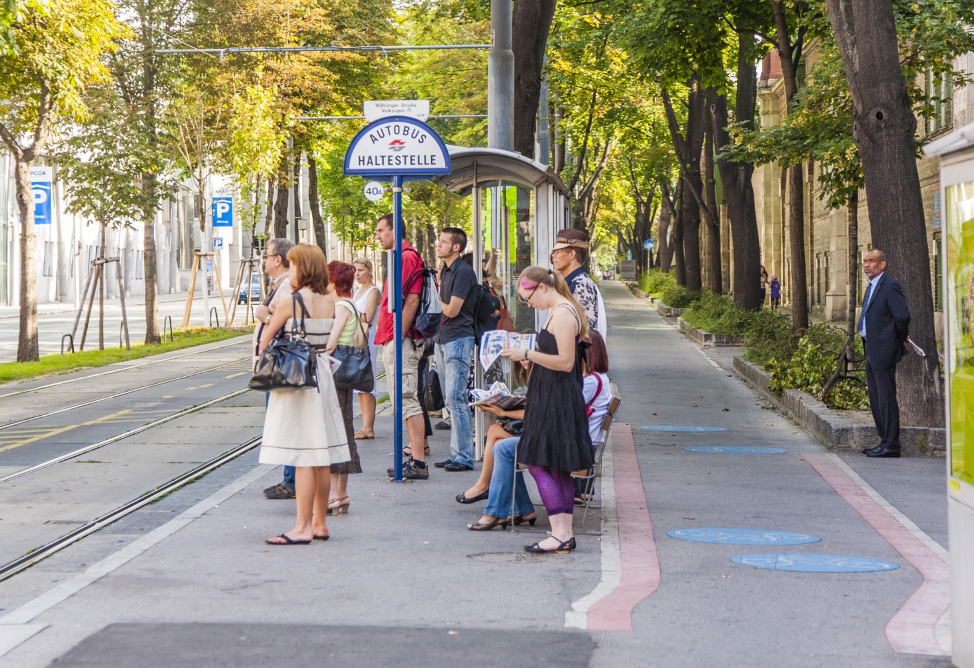 Eine Bim-Haltestelle in Wien am Ring. Einige wartende Fahrgäste warten dort an der Haltestelle.