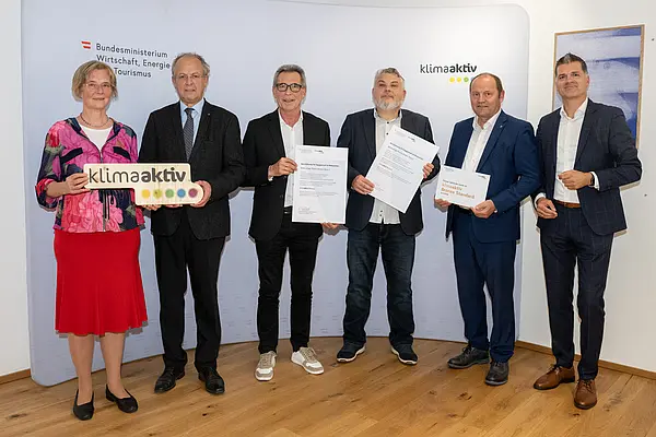 eine Gruppe von Menschen auf einer Bühne hält Urkunden in die Kamera