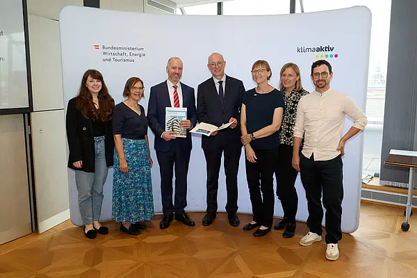 7 Personen mit Publikation in der Hand schauen in die Kamera